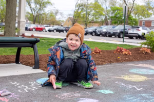 Boy in knit hat with chalk drawing on asphalt path